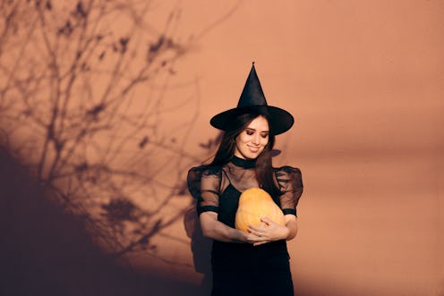 Halloween Woman in Witch Costume Holding Pumpkin. Party host organizing autumn holiday celebration i...