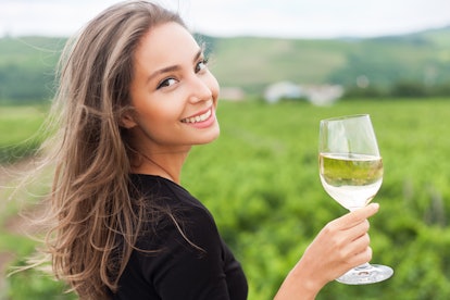 A young brunette woman smiling and holding up her glass of wine at a vineyard in the fall.