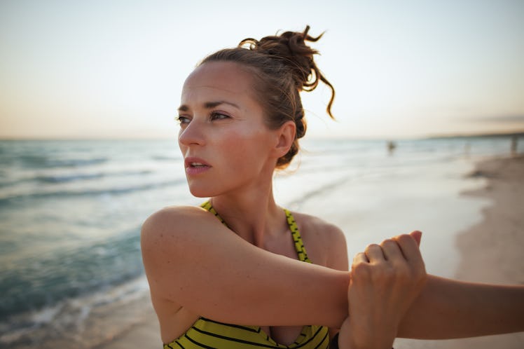 fitness woman in fitness clothes on the seacoast in the evening stretching.