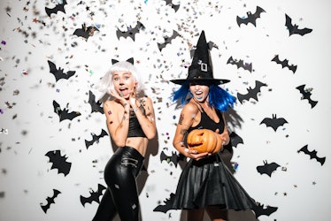 Two women dressed up for Halloween — one as a cat and one as a witch — smile as confetti falls aroun...