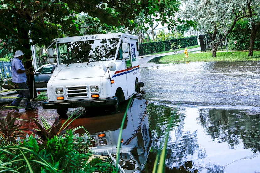 A postal worker returns to their truck parked on a flooded street a few miles from the downtown Miam...
