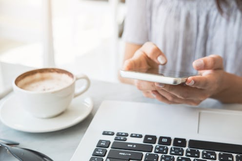 Young woman using smart phone and laptop with cup of coffee in cafe