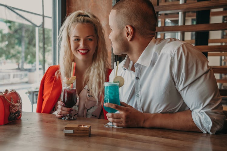 Young african man and blonde american woman drink cocktail, happy couple in bar drink cocktail and h...