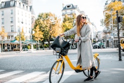 Portrait of a young stylish woman with yellow bicycle on the street in Paris