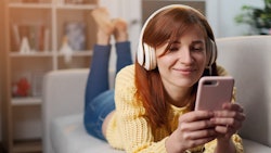 Cheerful young woman in headphones listening to music with his smartphone. Girl in headphones is lis...