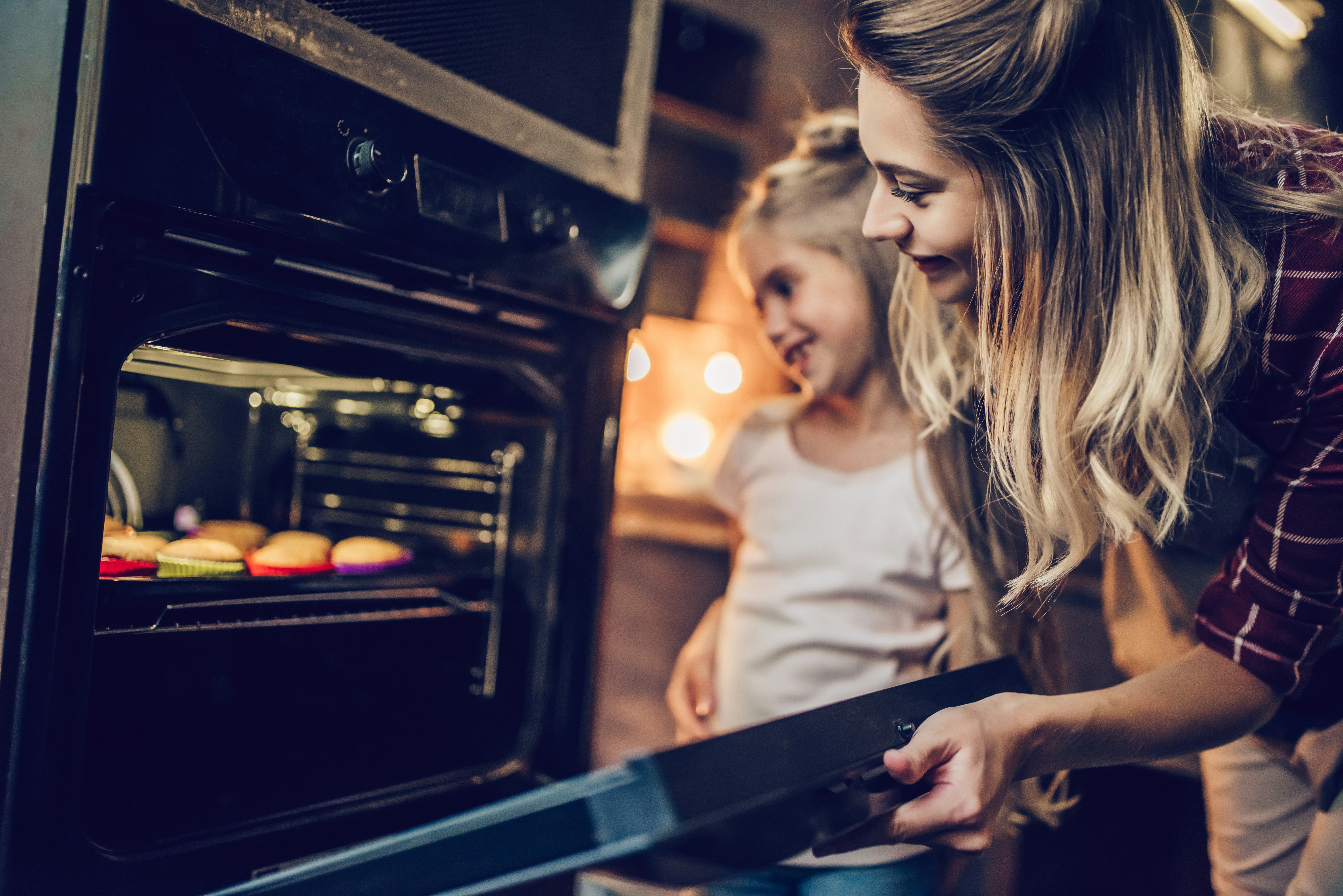 Attractive young woman with her little cute daughter are cooking cakes on kitchen.
