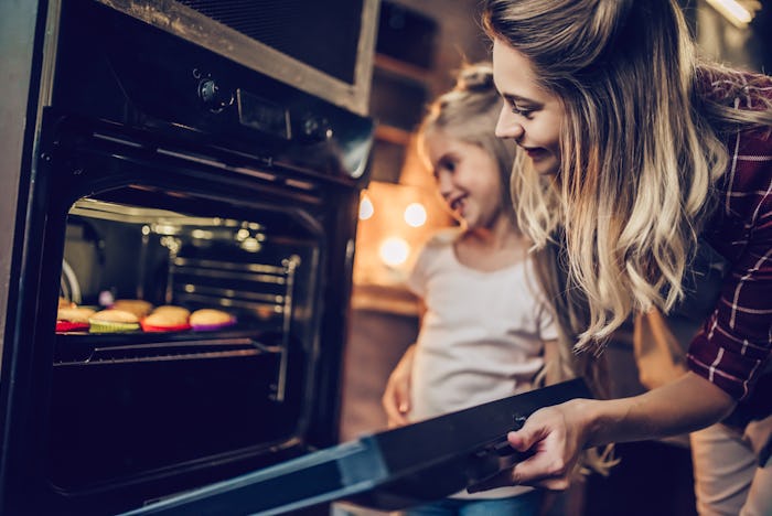 Attractive young woman with her little cute daughter are cooking cakes on kitchen.