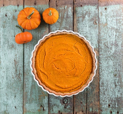 Thanksgiving dessert. Homemade rustic open pumpkin pie with small decorative pumpkins on shabby blue...