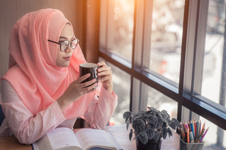 Arab women in hijab holding and drinking coffee cup sitting in the coffee shop