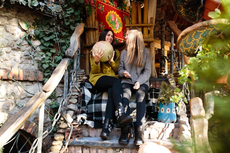 Two girls in sweaters, leggings, and boots sit on wooden steps in the fall.