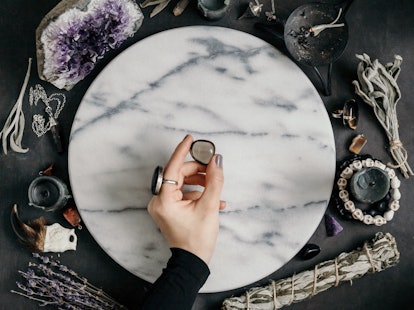 Witch's hand holding Smoky quartz above a marble white round tray. The place for witchcraft with mag...
