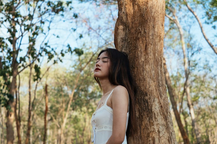 Girl closing her eyes leaning against a tree under shadow.