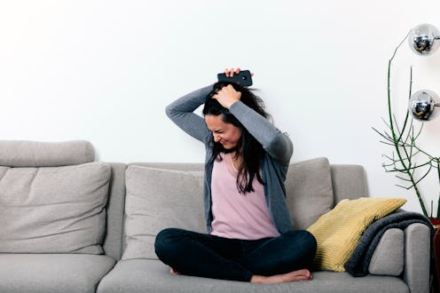 woman on a couch with angry and desperate face, holding a mobile phone and teraing her hair