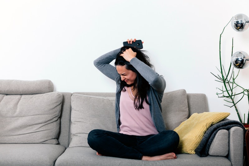 woman on a couch with angry and desperate face, holding a mobile phone and teraing her hair