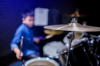 Selective focus to cymbals of drum set with blurry kid learning and play drum set with teacher in mu...