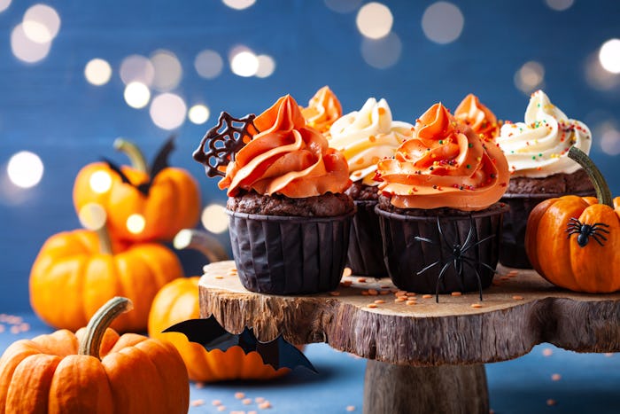 Halloween cupcakes and pumpkins on dark blue background. Sweets for holiday party.