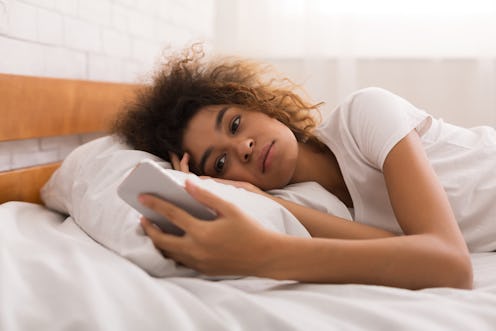 Woman looking unhappy at text message, lying in bed in the morning