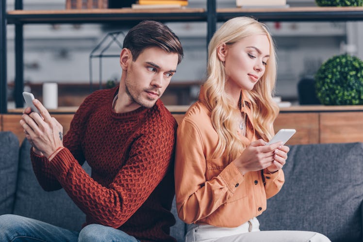 young couple sitting back to back and using smartphones, jealousy concept