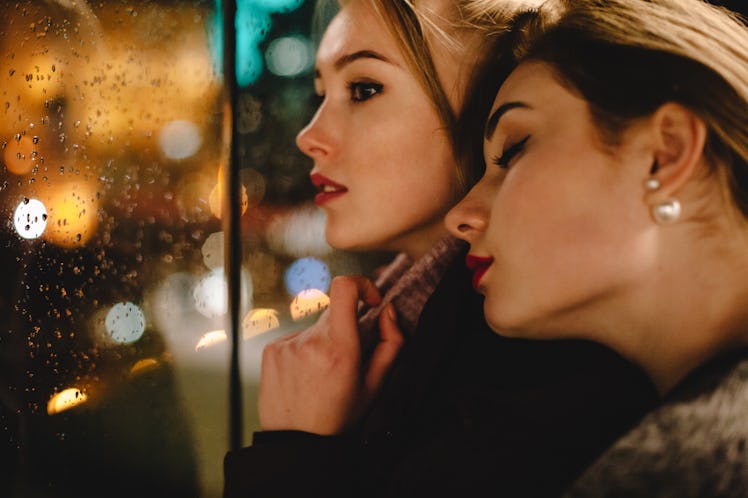 Lesbian couple romancing in city standing beside window during rain at night