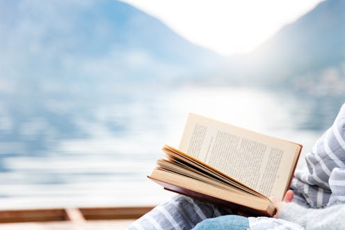 A woman reads a book of short stories while looking out at a winter landscape. 