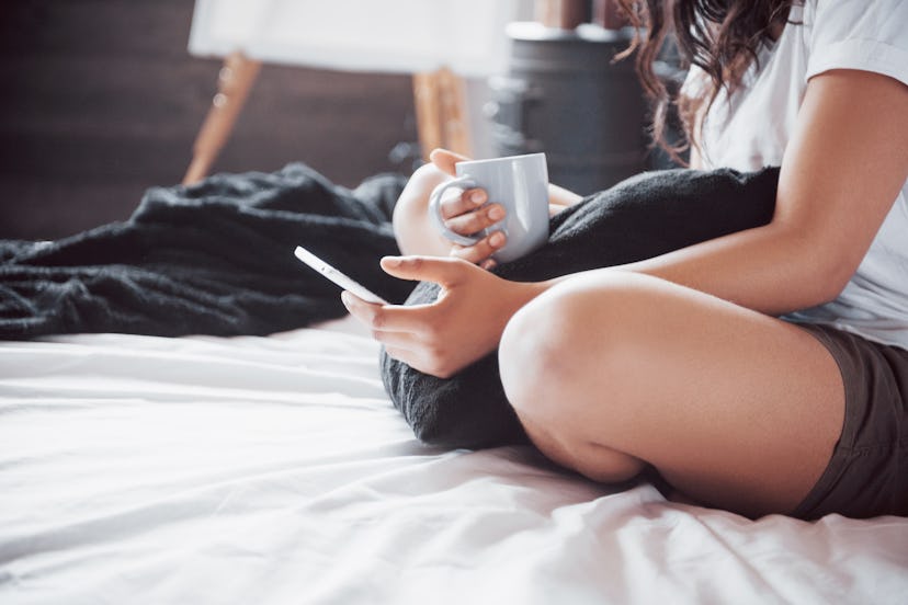 Portrait of beautiful woman waking up in her bed and looks into the phone. Check social networks, se...