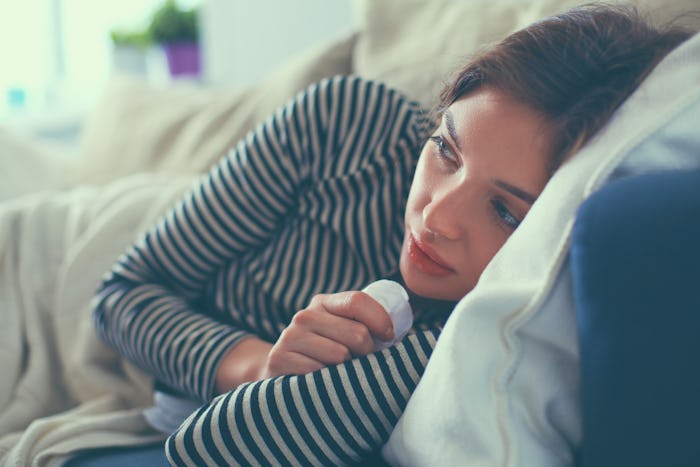 Portrait of a sick woman with the flu blowing her nose while sitting on the sofa