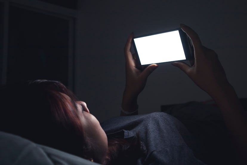 Asian woman using her mobile phone on the bed in dark room.