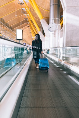 A brunette woman pulls her suitcase and walks on a moving walkway in an airport.