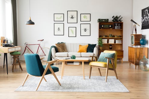 Stylish vintage furniture in a spacious flat interior with beige sofa, chairs and posters on the wal...