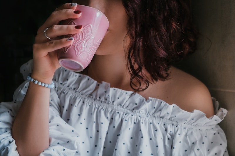 Close up young beautiful curly french woman drinking tea of coffee from a pink ceramic cup. Ginger t...