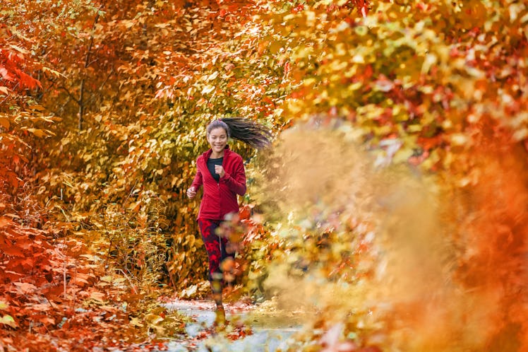 A brunette woman runs through the fall foliage on a jog.