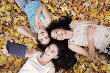 Unique perspective of three teenage girls taking picture with smartphone while lying down on autumn ...