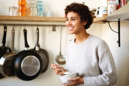 Portrait of smiling african american woman standing in kitchen eating breakfast cereal