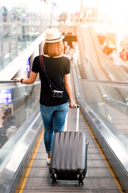 A woman dressed in jeans, a black T-shirt, and a hat pulls her suitcase in the airport.