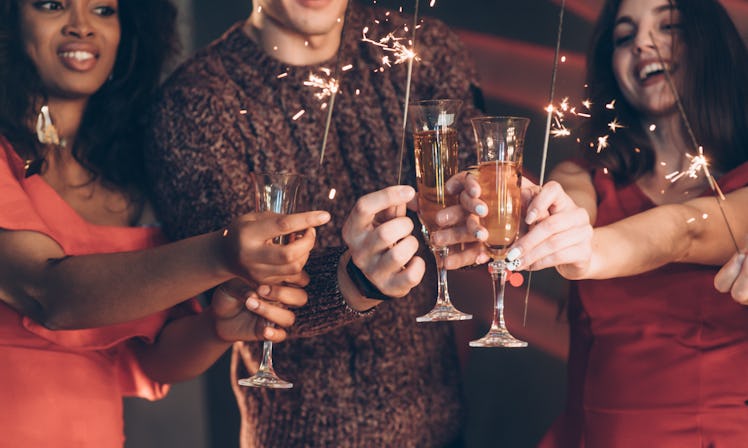 Half burned out. Multiracial friends celebrate new year and holding bengal lights and glasses with d...