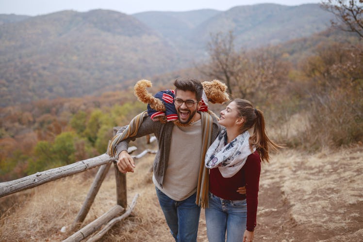 A cute couple dressed in casual clothes laughs and takes a walk in nature with their dog.