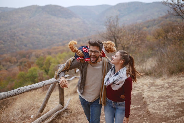 A cute couple dressed in casual clothes laughs and takes a walk in nature with their dog. 