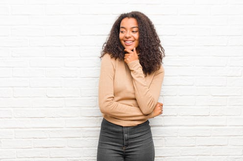 young black woman smiling with a happy, confident expression with hand on chin, wondering and lookin...