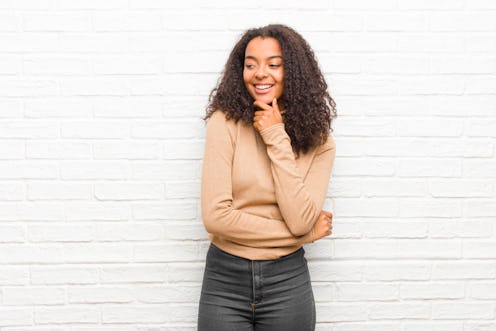 young black woman smiling with a happy, confident expression with hand on chin, wondering and lookin...