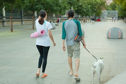 A young couple walks their dog, coming back from yoga, carrying their mats. 