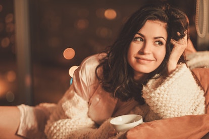 Portrait of beautiful young woman with cup of hot drink in cozy home interior.