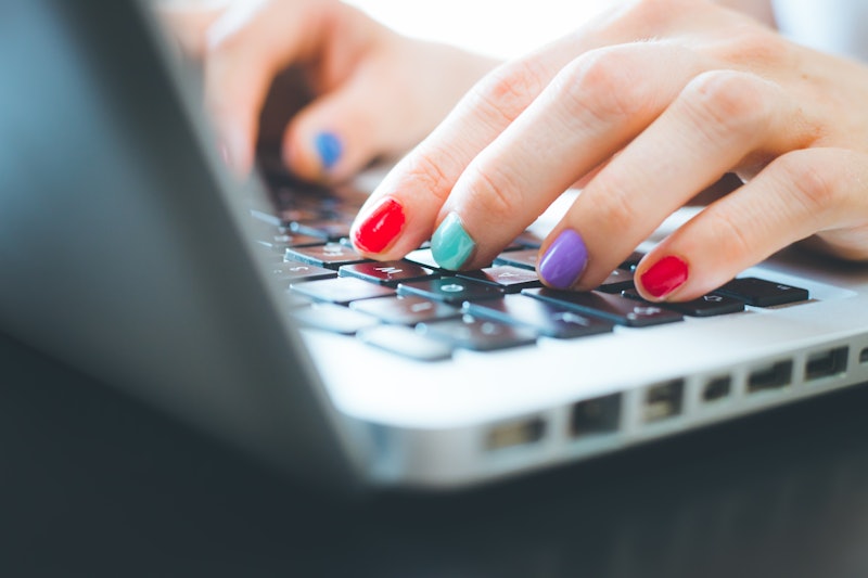 Woman fingers with colorful polished nails are typing on a laptop keyboard. Feminized leadership sty...