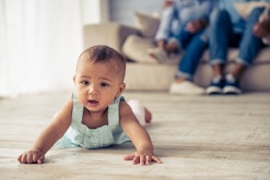 Adorable Afro American baby girl is looking forward with interest while crawling on wooden floor at ...