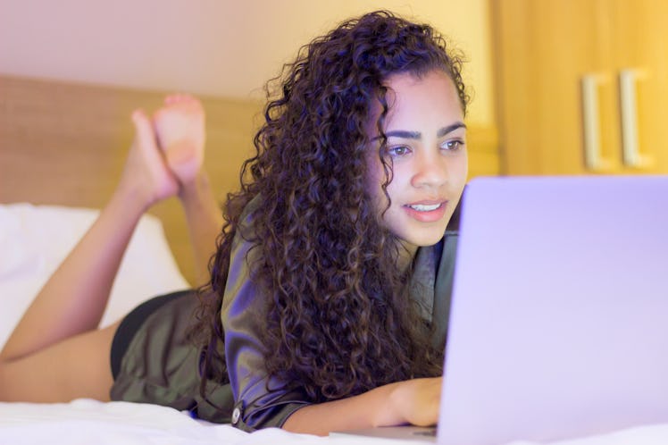 Pretty African woman using laptop computer in bed in room and smiling