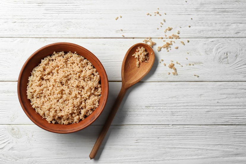 Cooked quinoa in bowl on white wooden background
