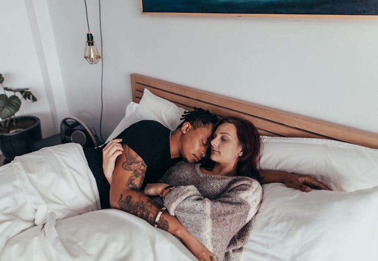 Young couple sleeping peacefully on the bed in bedroom. Man embracing woman while lying asleep.