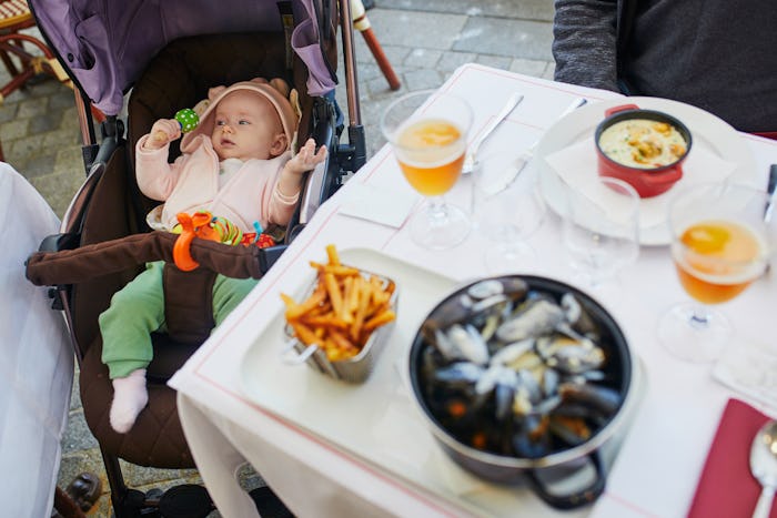 Cheerful baby girl in stroller near table in restaurant. Going out with kids. Boiled mussels in whit...
