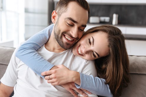 Image of couple in love man and woman in casual wear hugging together at home while sitting on sofa ...