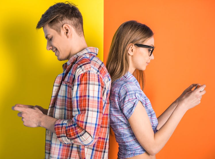 Portrait of young couple standing back to each other and looking at the phone.