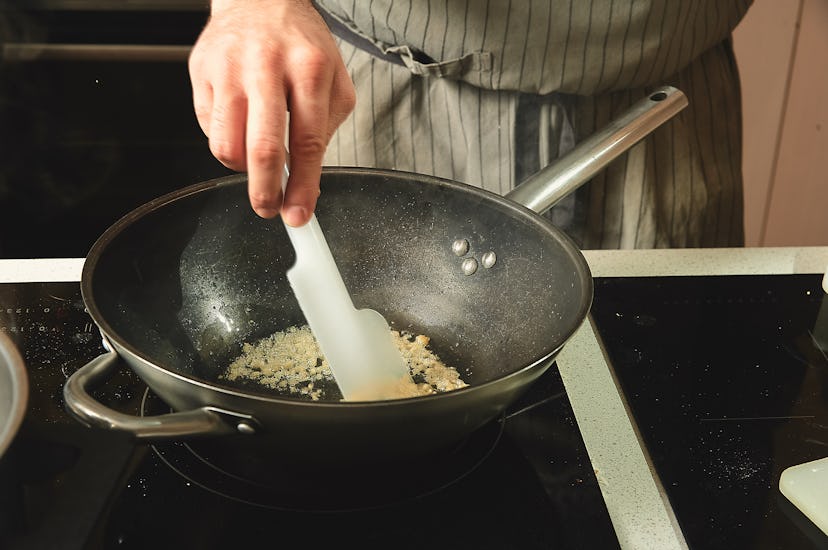 The chef fries finely chopped garlic for a wok of noodles, stirring with a plastic spatula.